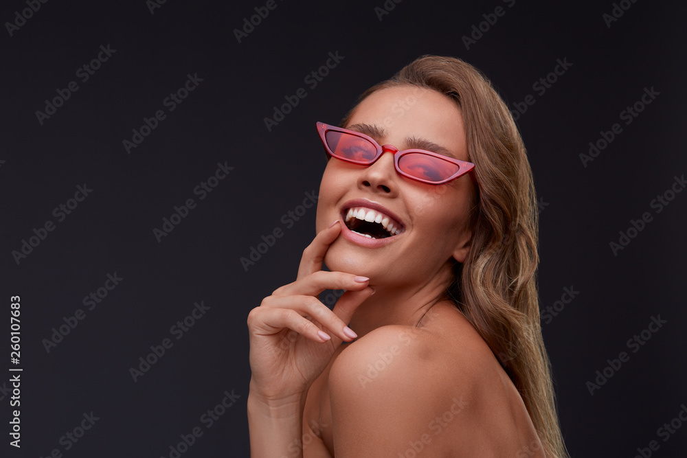 Portrait of beautiful young woman with perfect makeup wearing red sunglasses. Smiling fashion model in cat eye sunglasses posing on gray background. Studio shot. Summer vacation. Portrait of beautiful young woman with perfect makeup wearing red sunglasses. Smiling fashion model in cat eye sunglasses posing on gray background. Studio shot. Summer vacation.