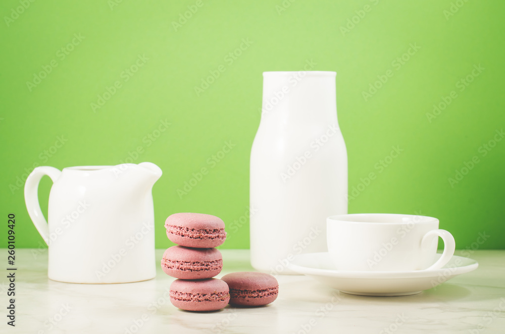 sweet macaroons or macaron, coffee cup, white creamer and bottle on a green background. French dessert sweet macaroons or macaron, coffee cup, white creamer and bottle on a green background. French dessert