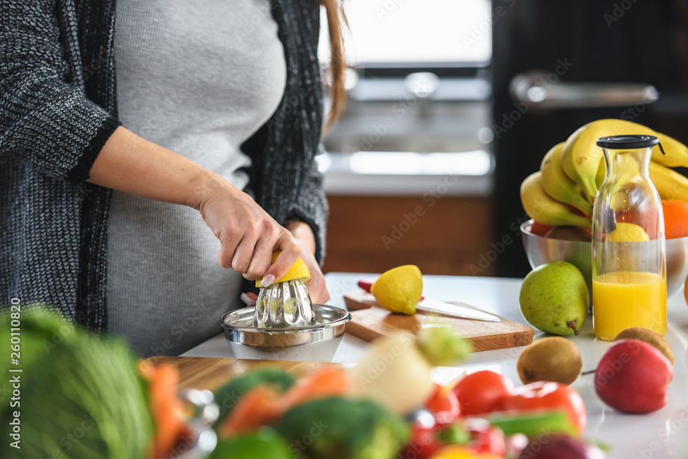 Pregnant woman preparing healthy food with lots of fruit and vegetables at home. Close-up.