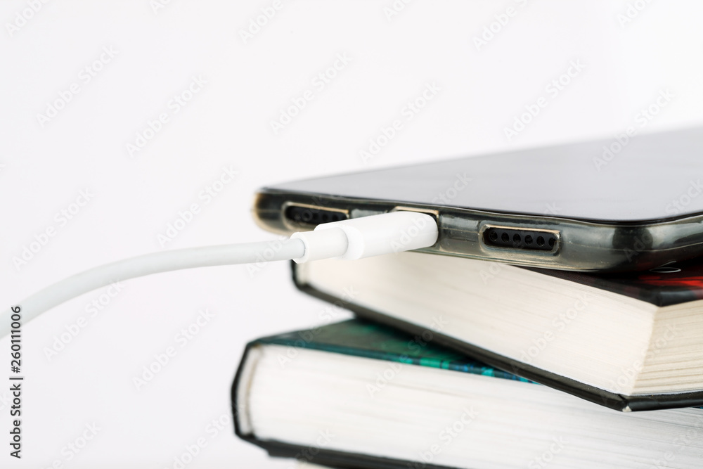 Charging smartphone on heap of books on a white background Charging smartphone on heap of books on a white background