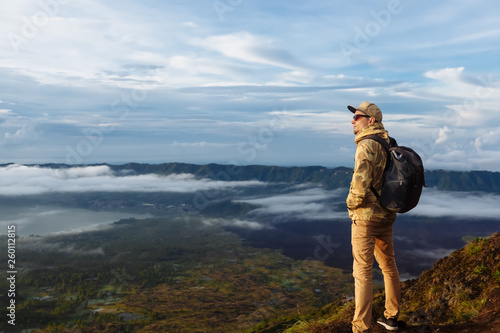 Man tourist looks at the sunrise on the volcano Batur on the island of Blai in Indonesia. Hiker man with backpack travel on top volcano, travel concept