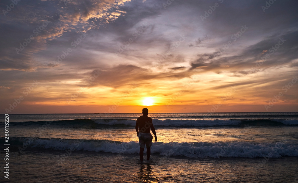 A man walks into the water at sunset