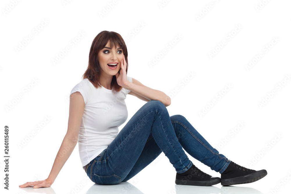 Happy Young Woman Is Sitting On Floor, Looking Away And Talking. Side View. Happy Young Woman Is Sitting On Floor, Looking Away And Talking. Side View.
