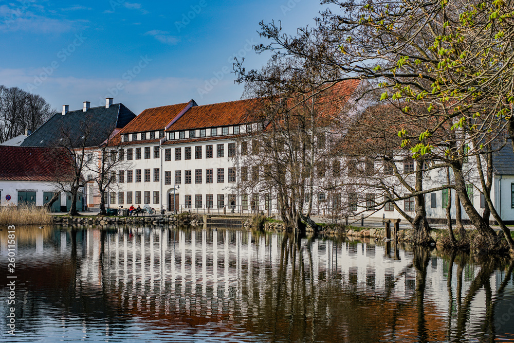 Historical buildings at Brede in Lyngby, Denmark, reflecting in the almost still water.