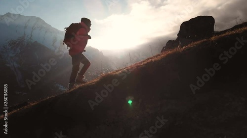 Aerial view of epic shot of a girl walking on the edge of the mountain as a silhouette in a beautiful sunset. Silhouette of a girl in a hat with a backpack climbing uphill