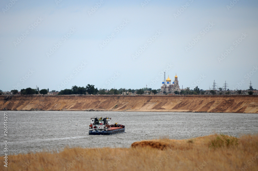 Fototapeta premium The ship sails on the river. On the shore stands the Orthodox Church
