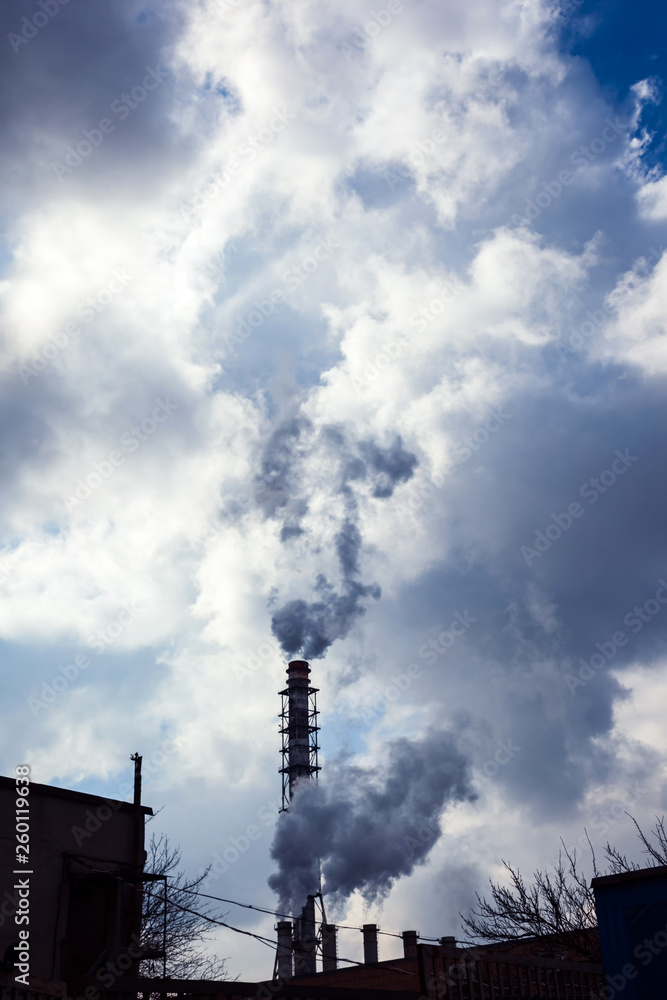 Industrial pipes smoke and release white smoke into the sky with clouds. Air pollution and harmful emissions from poor ecology of the environment and global warming.