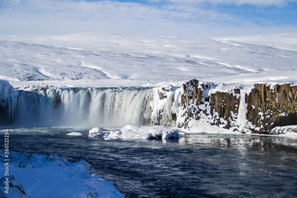 Scenic landscape view of tourist popular attraction Godafoss waterfall in northern Iceland in winter time. Long exposure falling water photo, snow covered mountains on background. 