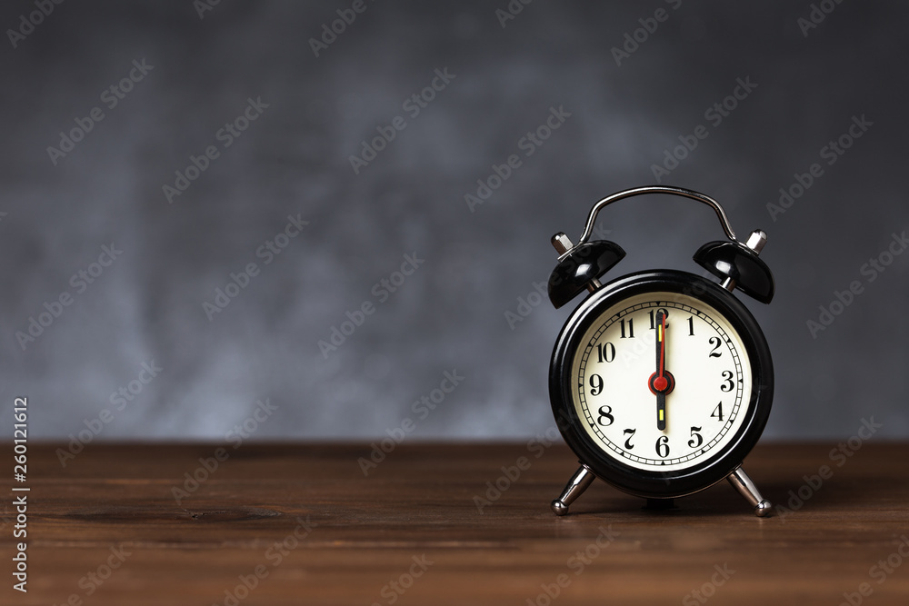 Clock hand at 6 o'clock alarm at 6 o'clock. Vintage / retro black analog alarm clock on wooden table with copy space on dark background Clock hand at 6 o'clock alarm at 6 o'clock. Vintage / retro black analog alarm clock on wooden table with copy space on dark background