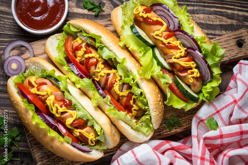 Hot dog with sausage and vegetables on wooden table.