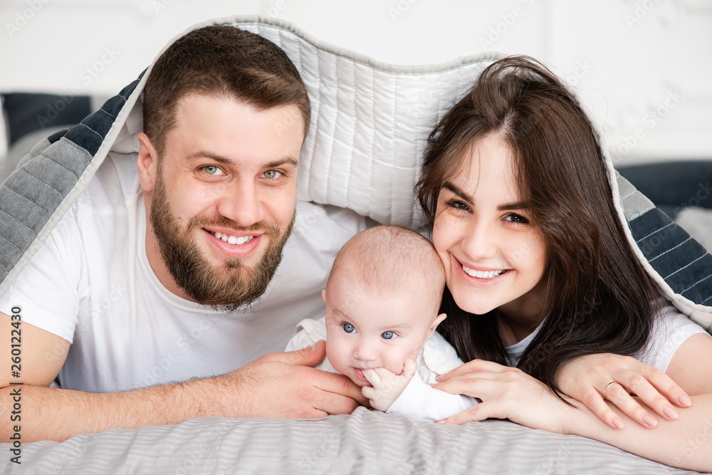Young smiling family with daughter under blanket Young smiling family with daughter under blanket