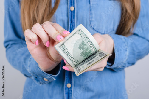 Cropped close-up photo of girlish beautiful hands with long nails pink bright manicure on fingers holding calculating old money wearing denim clothes isolated grey background