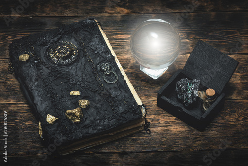 Fototapeta Crystal ball and a magic book on a wizard table background.
