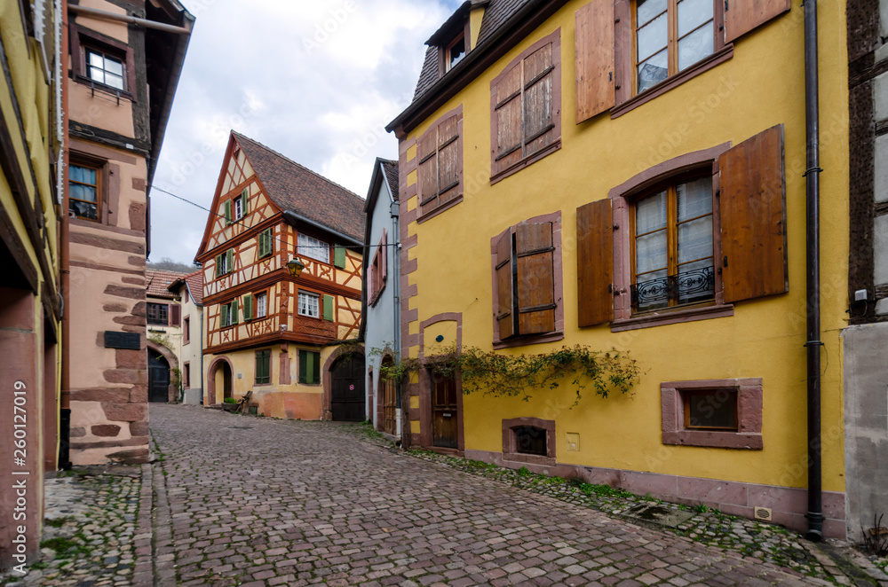 View of the street with old half-timbered houses in a small town. Kaysersberg. Alsace. France. In the foreground there is a house of bright yellow color.