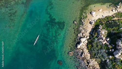 Aerial drone bird's eye view of sport canoe operated by team of young women in tropical caribbean exotic island with emerald and sapphire clear sea
