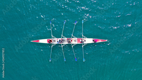 Aerial drone bird's eye view photo of red sport canoe operated by team of young men and women in emerald clear sea