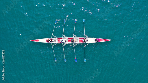 Aerial drone bird's eye view photo of red sport canoe operated by team of young men and women in emerald clear sea