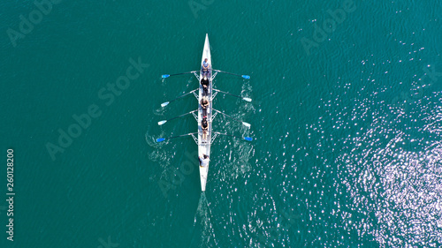 Aerial drone bird's eye view of sport canoe operated by team of young men and women in open ocean sea