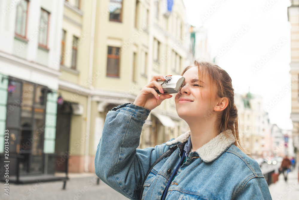 Portrait of a tourist girl takes a photo of architecture on a retro film camera, wearing a denim jacket, standing on the street of the town. Tourist photographs sights in a European town. Copyspace Portrait of a tourist girl takes a photo of architecture on a retro film camera, wearing a denim jacket, standing on the street of the town. Tourist photographs sights in a European town. Copyspace