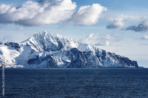 Snow peaks, glaciers and rocks of Aleutian islands in sunny winter day as viewed from ship passing in calm sea