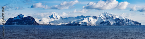 Snow peaks, glaciers and rocks of Aleutian islands in sunny winter day as viewed from ship passing in calm sea