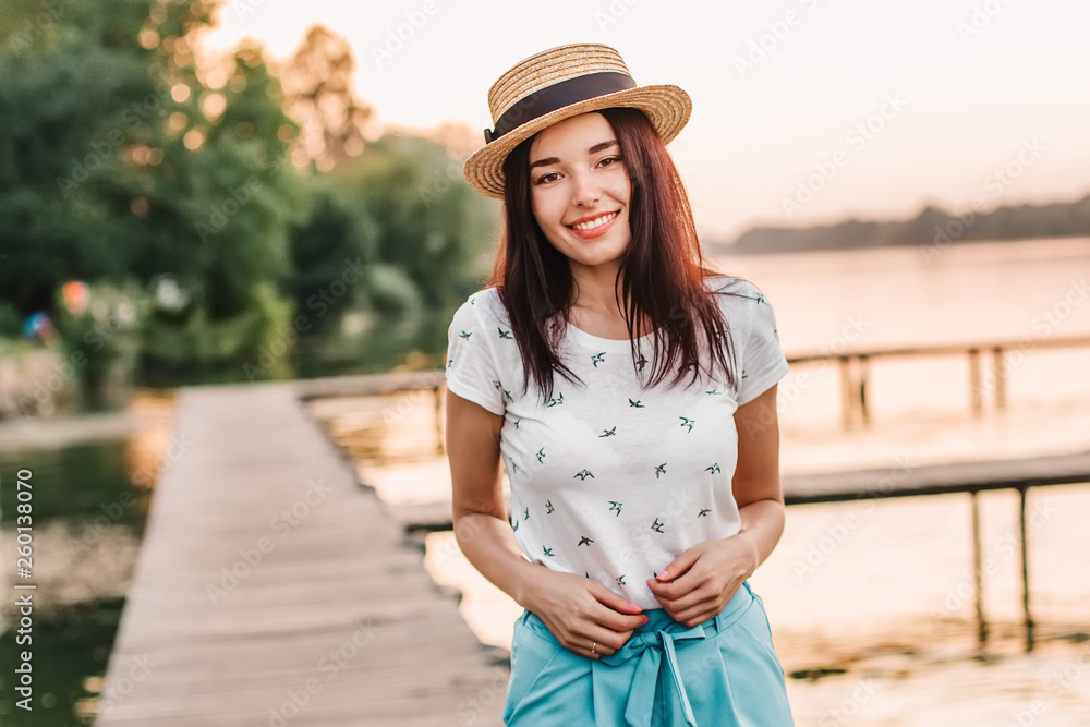 Obraz premium Beautiful young woman walking on pier at sunset in summer.