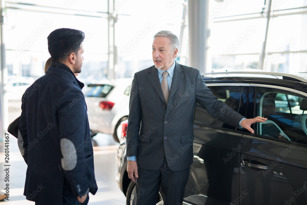 Happy young family talking to the salesman and choosing their new car in a showroom Happy young family talking to the salesman and choosing their new car in a showroom