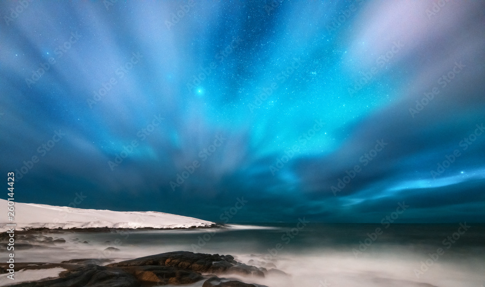 Amazing aurora borealis. Northern lights in Teriberka, Russia. Starry sky with polar lights and clouds. Night winter landscape with aurora, sea with stones in blurred water, snowy mountains. Travel