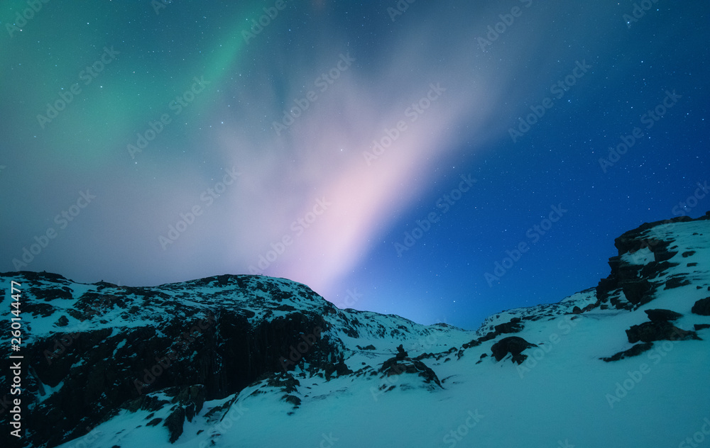 Naklejka premium Aurora borealis above the snow covered mountain range in europe. Northern lights in winter. Night landscape with green polar lights and snowy mountains. Starry sky with aurora. Nature. Space