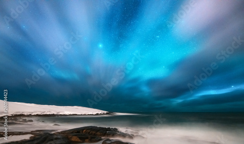 Amazing aurora borealis. Northern lights in Teriberka, Russia. Starry sky with polar lights and clouds. Night winter landscape with aurora, sea with stones in blurred water, snowy mountains. Travel © den-belitsky