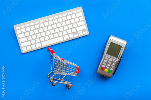 buying products with card machine, keyboard and mini trolley on blue background top view