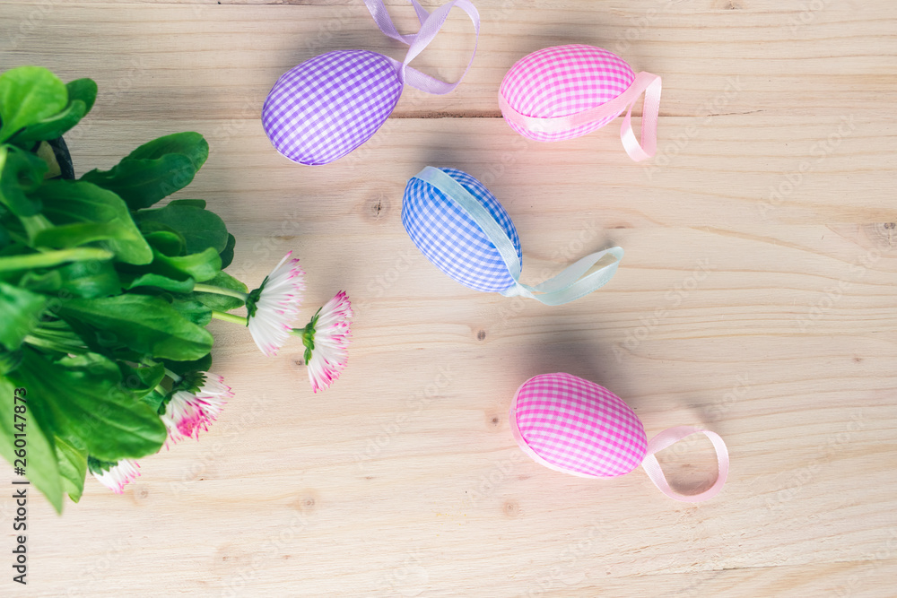 Top view of pastel pink and blue checkered Easter eggs decorations and blooming pink and white daisies on pale wooden background. Easter eggs and spring flowers background Top view of pastel pink and blue checkered Easter eggs decorations and blooming pink and white daisies on pale wooden background. Easter eggs and spring flowers background