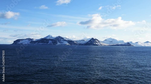 Snow peaks, glaciers and rocks of Aleutian islands in sunny winter day as viewed from ship passing in calm sea