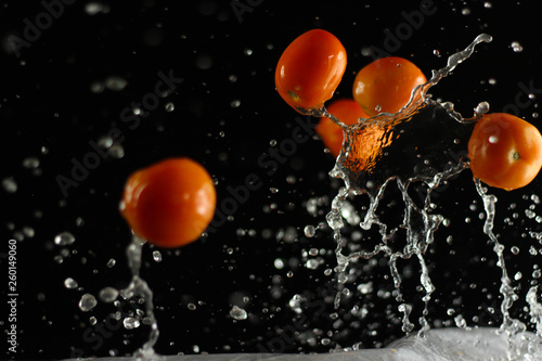 Fresh tomato dropped into water, isolated on dark background
