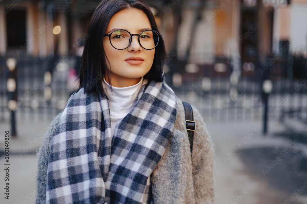 Attractive young girl wearing glasses in a coat walking on a sunny day