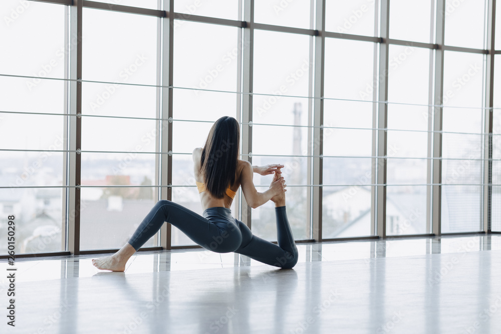Fototapeta premium young attractive girl doing fitness exercises with yoga on the floor against the background of panoramic windows