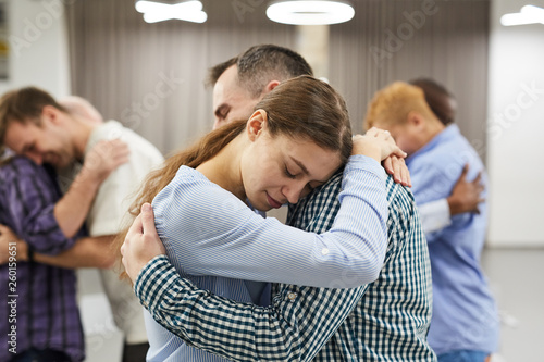 Waist up portrait of people hugging during group therapy session, focus on smiling young woman in foreground