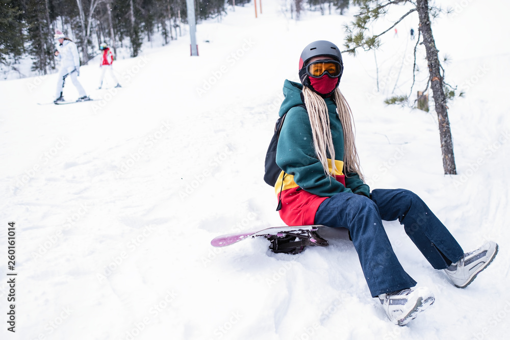 Young woman snowboarder freerider sitting in the mountains on a snowy slope.