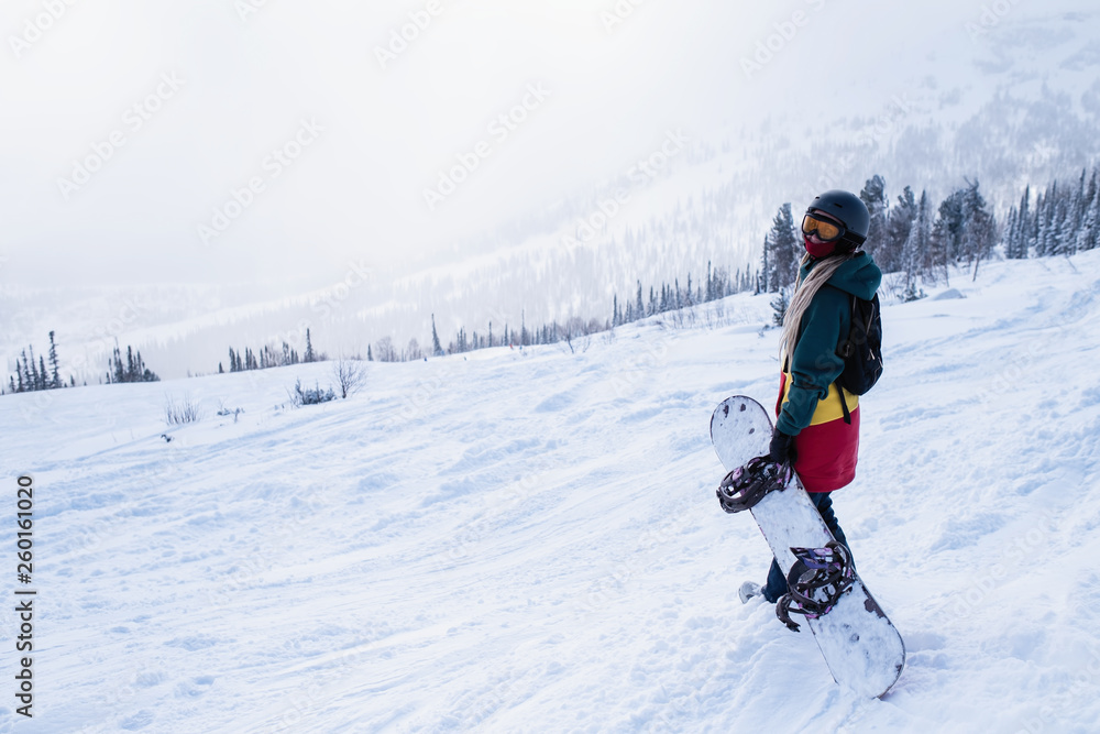 Female snowboarder freerider goes to the mountains holding a snowboard.
