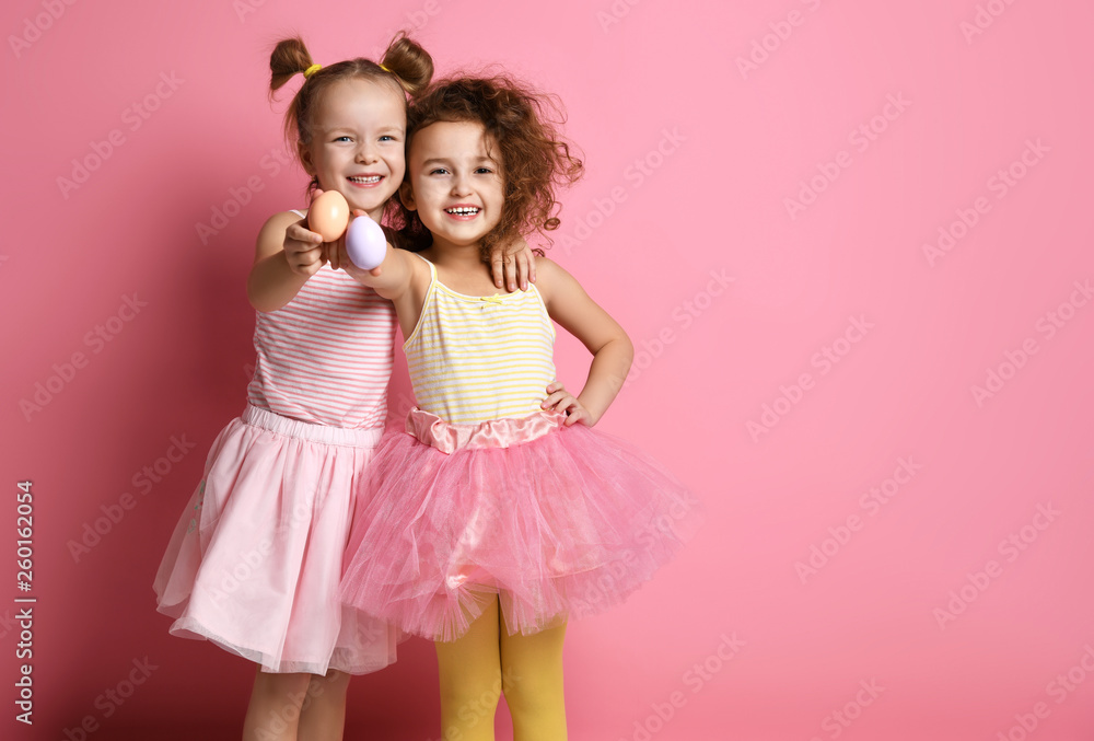 Two happy smiling kids girls in colorful clothes demonstrate painted eggs on Easter day Two happy smiling kids girls in colorful clothes demonstrate painted eggs on Easter day