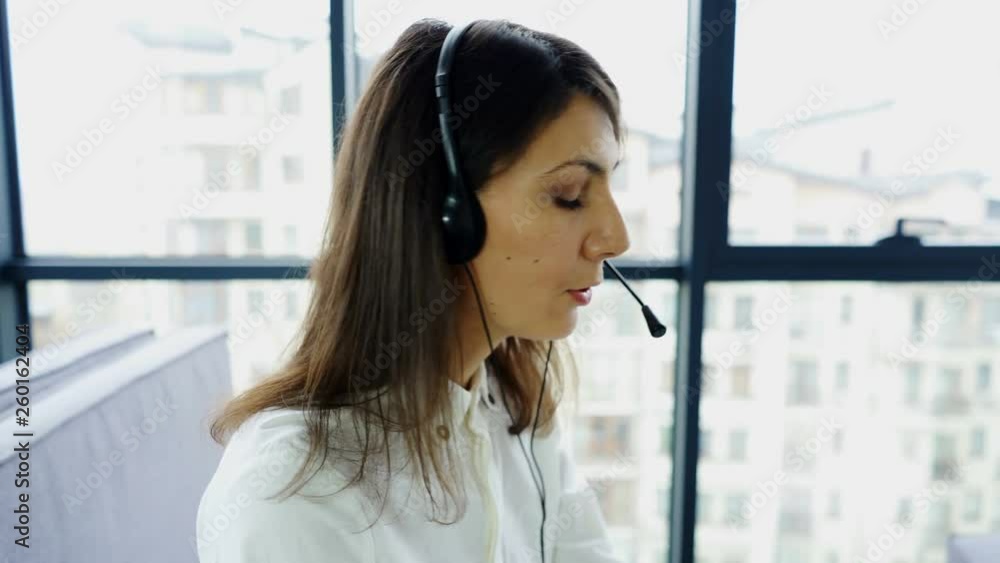 4K. Office call center work. Woman operator in earphones answer client, slider shot