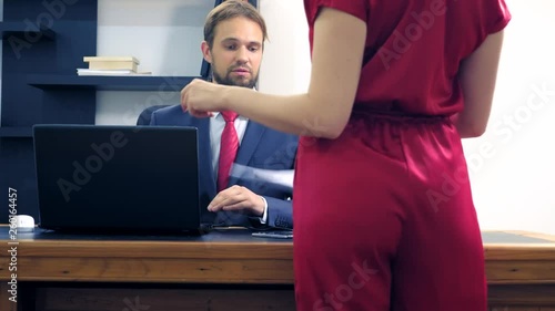 Office flirt. Attractive woman in red overalls with a deep neckline flirting at the table with her colleague. man looks at the chest of a woman in the office