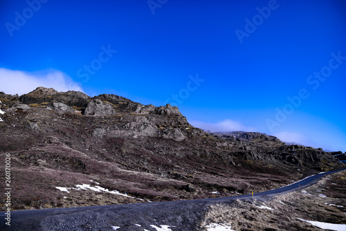 The peak of a smaller mountain with clouds covering parts of the mountains, and a lonely road
