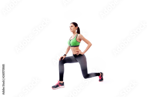 A young woman model in a sporty short top and gym leggings makes lunges  by the feet forward, hands are held out to the side   on a  white isolated background in studio © Виталий Сова