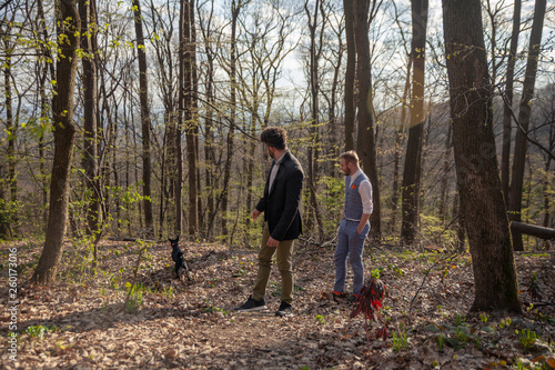 two men, young gay couple walking in forest with their dog.