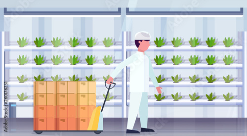 man agriculture engineer in uniform carrying pallet truck with cardboard boxes modern organic vertical farm interior green plants growing farming industry concept horizontal flat