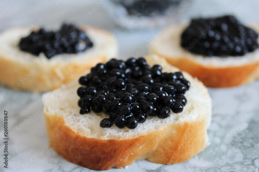 Top view of Tasty Sandwich with black caviar on White marble background. .Free space for text. Black caviar. Luxurious culinary delicacy. Top view of Tasty Sandwich with black caviar on White marble background. .Free space for text. Black caviar. Luxurious culinary delicacy.
