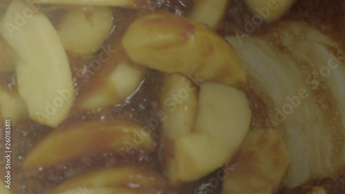 A close up of fresh apple pieces stirring into hot sizzling caramel mixture. Preparation for making Apple Tarte Tatin