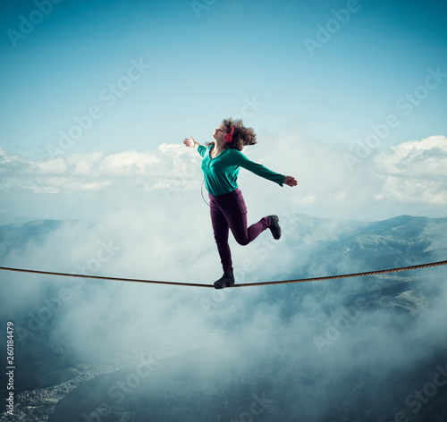 Woman balancing on a rope above clouds and mountains , while listening music . The concept of freedom.