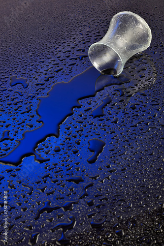 Glass of water spilled with drops on light background